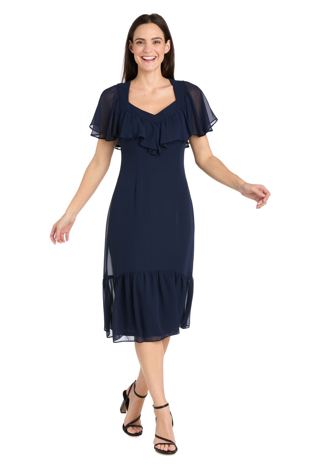 A woman stands against a white background wearing the R&M Richards 4054P Petite Navy Blue Midi Party Dress with short sleeves, ruffle details, and black strappy heels.